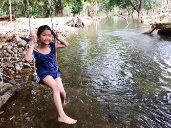 Portrait of smiling girl sitting on swing over river