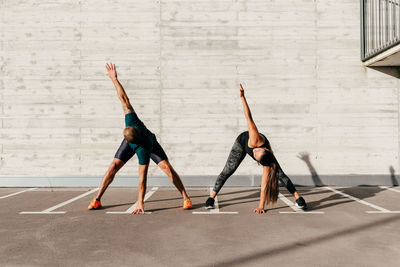 Calm sportsman and sportswoman stretching body bending forward with closed eyes before training