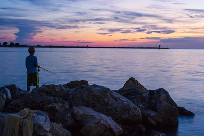 Rear view of man fishing in sea against sky