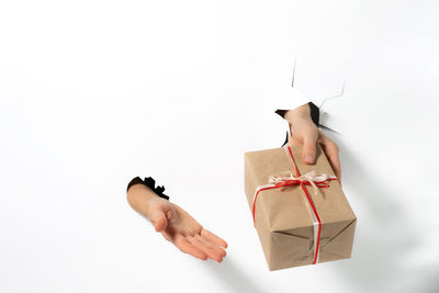 Close-up of female hand holding gift with ribbon through a torn white paper. creative present