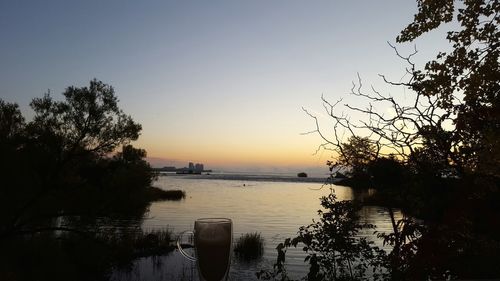 Silhouette trees by river against clear sky during sunset