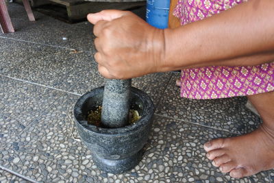 Low section of woman grinding spices in mortar and pestle on floor