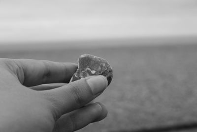 Close-up of hand holding stone against cloudy sky