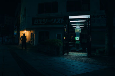 Person on illuminated footpath by building at night