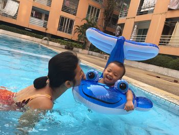 Mother with daughter swimming in pool against buildings