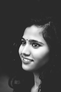 Close-up portrait of smiling young woman against black background