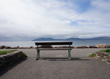 Empty bench on beach against sky