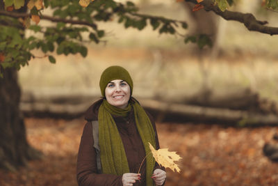 Portrait of smiling woman holding autumn leaf standing at park