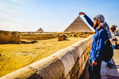 Optical illusion of man touching pyramid against clear sky