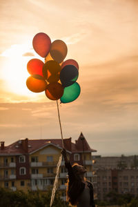 Rear view of silhouette person holding balloons against sky during sunset