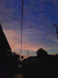 Silhouette trees by street against sky during sunset