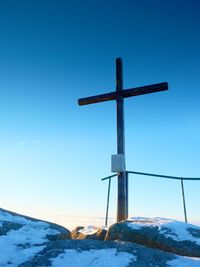 Cross on snow covered landscape against clear blue sky