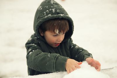 Close-up of cute boy playing with snow during winter