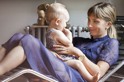 Mother playing with baby while sitting on lounge chair at home