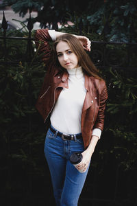 Portrait of beautiful young woman holding coffee cup while standing against plants
