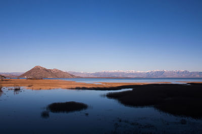 Scenic view of lake and mountains against clear blue sky