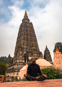 Low angle view of man with eyes closed meditating against temple