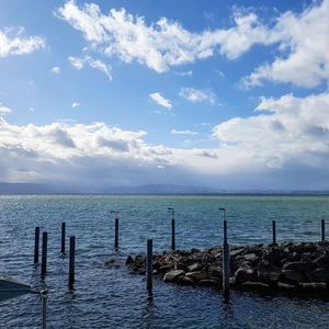 Wooden posts in sea against sky