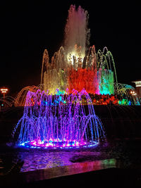 Firework display over illuminated fountain against sky at night