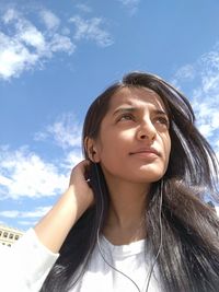 Close-up of young woman listening to music on headphones against sky