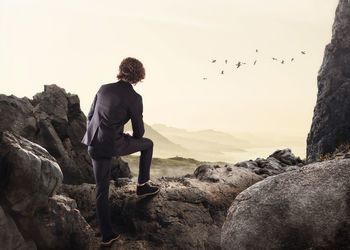 Man standing on rock looking at mountains against sky