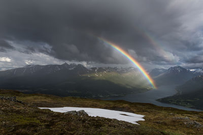 Scenic view of rainbow over mountains during stormy weather