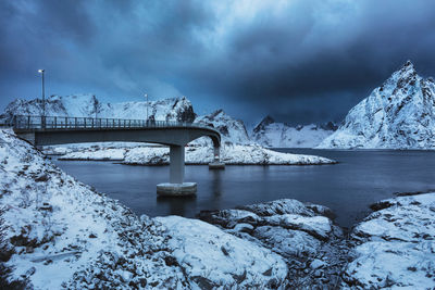 Bridge over lake amidst snowcapped mountains against cloudy sky during winter