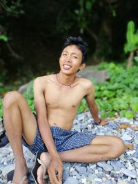 Portrait of smiling shirtless young man sitting on pebble stones