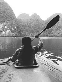 Rear view of man sitting on lake against mountain