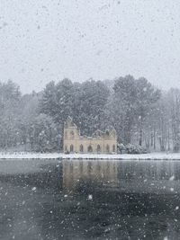 Frozen building by trees against sky during winter