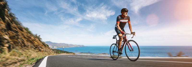 Man riding bicycle on road by sea against sky