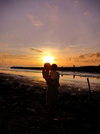 Friends standing on beach against sky during sunset
