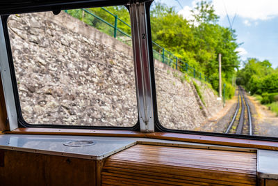 A view from the window of a moving train, visible tracks, trees and blue sky with white clouds.