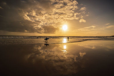 Silhouette people on beach against sky during sunset