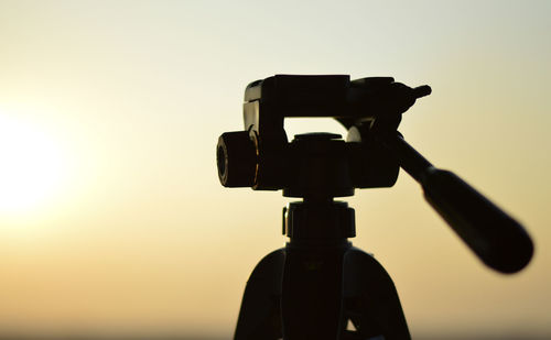 Close-up of silhouette camera against sky during sunset