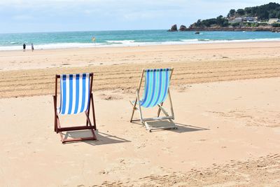 Deck chairs on beach against sky