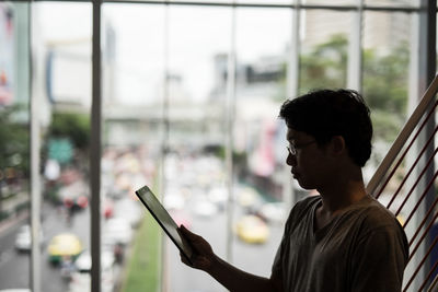 Portrait of young man using mobile phone against window