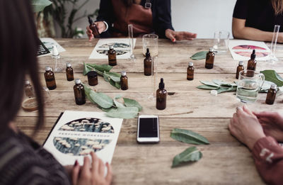 High angle view of multi-ethnic female coworkers preparing perfume at wooden table in workshop