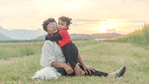 Portrait of grandmother with granddaughter on grassy land against sky at sunset