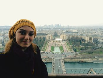 Portrait of young woman standing at railing in eiffel tower against cityscape