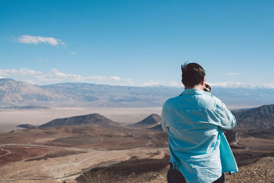 Rear view of man photographing landscape against sky