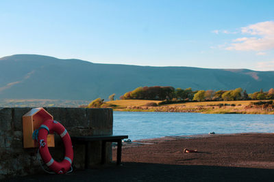 Man sitting on chair by lake against sky