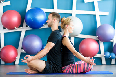 Side view of man and woman meditating while sitting on exercise mat