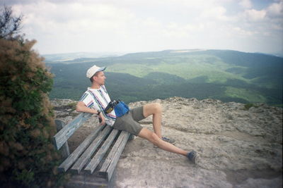 Full length of man sitting on mountain against sky