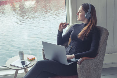 Woman using mobile phone while sitting on window