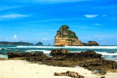 Rock formation on beach against blue sky