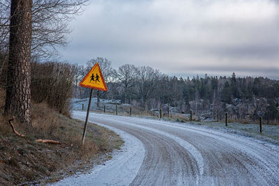 Road sign by trees against sky during winter