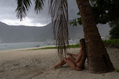 Woman by tree trunk at beach against sky