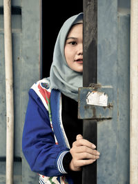 Portrait of young woman wearing hijab while standing by gate