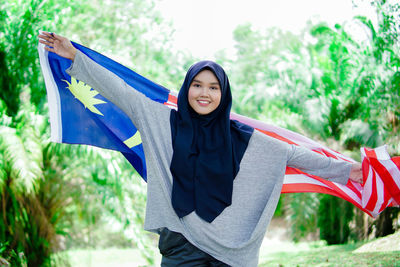 Portrait of young woman standing against trees